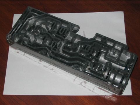 1991 Ford Bronco - A transmission valve body, a complex component with many internal passages, is shown on a white sheet of paper.