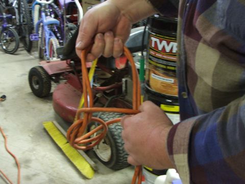 1965 Ford Mustang - A person's hands are holding an orange extension cord in front of a red lawn tractor. In the background, several bicycles are visible.