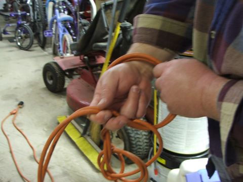 1965 Ford Mustang - A person is holding an orange extension cord in front of a red lawnmower and several bicycles.