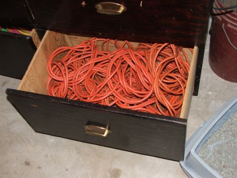 1965 Ford Mustang - A dark wooden drawer is filled with a tangled mess of orange extension cords, suggesting a storage area for electrical equipment.