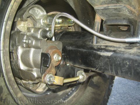 1990 Ford Bronco - close-up of a vehicle's rear axle showing a brake caliper, mounting bracket and a braided stainless steel brake line.