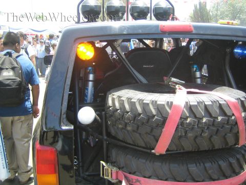 1990 Ford Bronco - open rear of an off-road race truck showing strapped-in spare tires, roll cage, light bar and a MasterCraft seat.