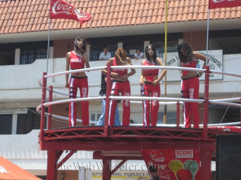 1990 Ford Bronco - Four promotional models in matching red Coca-Cola outfits stand on a railed red platform in front of a building.