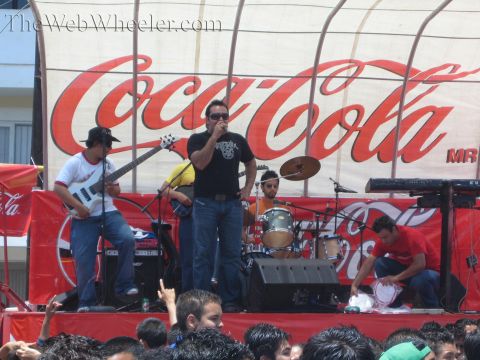 1990 Ford Bronco - band performs on stage in front of a large red Coca-Cola backdrop, with a singer, bassist and drummer above a crowd.