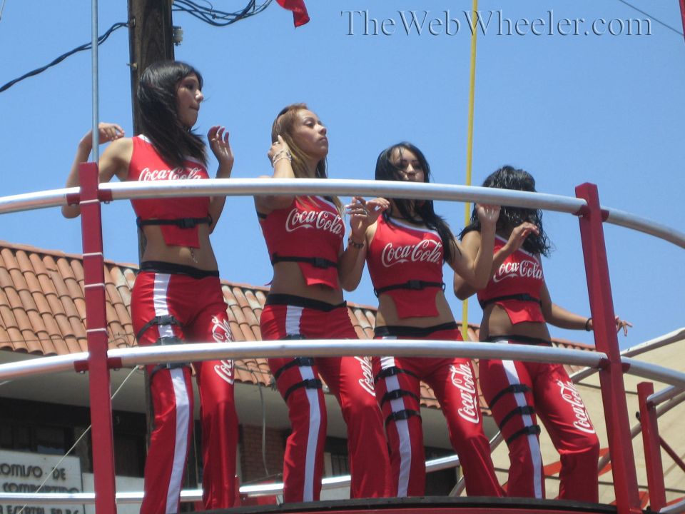 Four women in red Coca-Cola outfits on a railed red platform against a blue sky