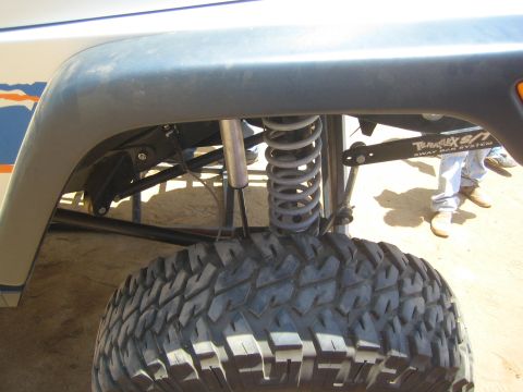 1990 Ford Bronco - close-up of an off-road vehicle's front suspension showing a coilover shock, Teraflex link arm, and a large knobby mud tire.
