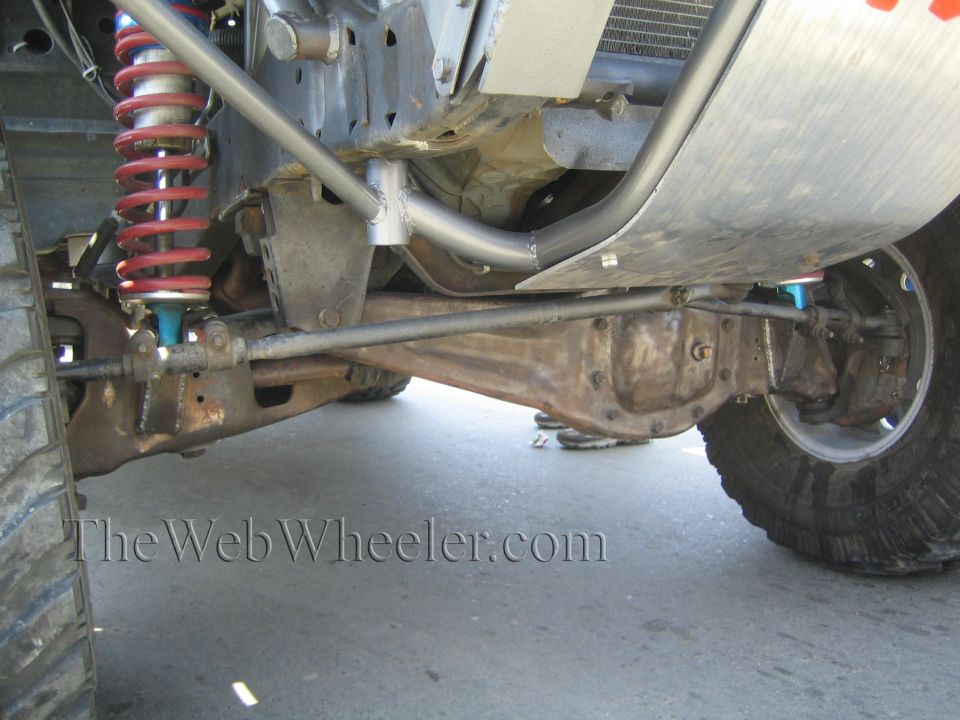 Undercarriage of off-road vehicle showing solid axle, red coilover, and steering link