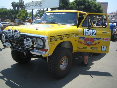1990 Ford Bronco - yellow vintage Ford Bronco off-road race truck numbered 1502 with Hella lights and BFGoodrich tires parked on a street.