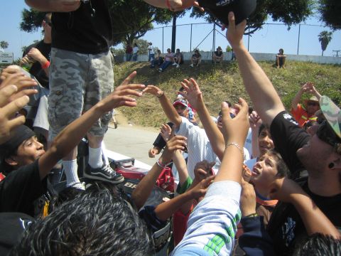 1990 Ford Bronco - crowd of children and teens reach up with outstretched hands toward items being tossed at an outdoor event near a fence.