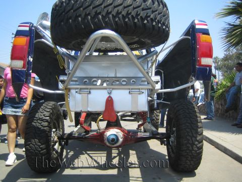 1990 Ford Bronco - rear of a lifted off-road vehicle reveals a chrome tube structure, mounted spare tire and exposed rear differential.