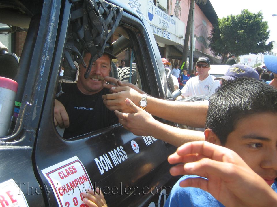 Driver in race truck cab shaking hands with fans, door reads Don Moss