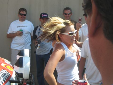 1990 Ford Bronco - blonde woman in sunglasses and a white tank top stands among a crowd of men outdoors, one capturing her on a camera phone.