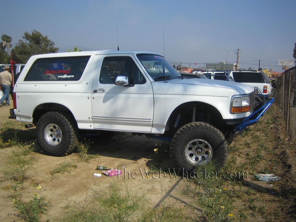 White lifted Ford Bronco with blue tube bumper parked in a dirt lot