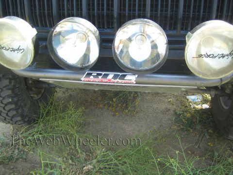 1990 Ford Bronco - close-up of a dark off-road vehicle's front bar holding four Lightforce driving lights with an RDC decal above weeds.