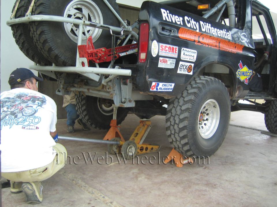 Man kneeling beside lifted black Ford Bronco with West Coast Broncos and River City Differential graphics on a jack