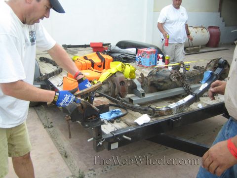 1990 Ford Bronco - Men in a shop work on a leaf-spring rear axle assembly secured to a black trailer with tools and gear scattered around.