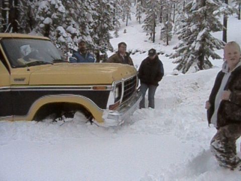 1979 Ford Bronco - A 1979 Ford Bronco is stuck in deep snow in a wooded area, with several people standing around it.