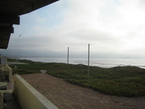 1990 Ford Bronco - hazy coastal ocean view over green ground-cover dunes and a brick patio, framed by a building eave with two poles.
