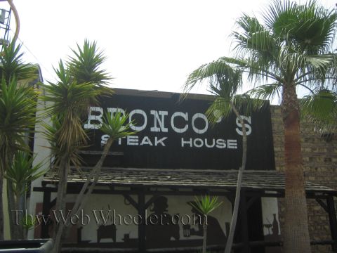 1990 Ford Bronco - large dark sign reading Bronco's Steak House sits atop a rustic building framed by palm and yucca plants.