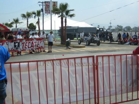 1990 Ford Bronco - off-road race car runs a street course behind a red Tecate-branded barrier as spectators and palms line the road.