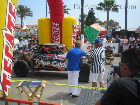 1990 Ford Bronco - red off-road race truck numbered 1625 lettered Felipe Calderon waits at a Tecate inflatable arch as officials and crowd watch.