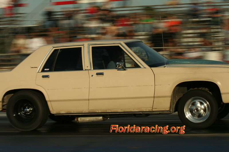 Tan sedan with a dark hood, seen from the side at a drag strip