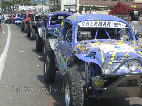 1990 Ford Bronco - Purple off-road race Beetle 554 lettered Shermak with BFGoodrich livery leads a row of staged race cars.