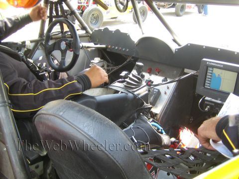 1990 Ford Bronco - Cockpit of a tube-frame off-road racer with a driver at the wheel, bucket seats and a Lowrance GPS unit on the dash.