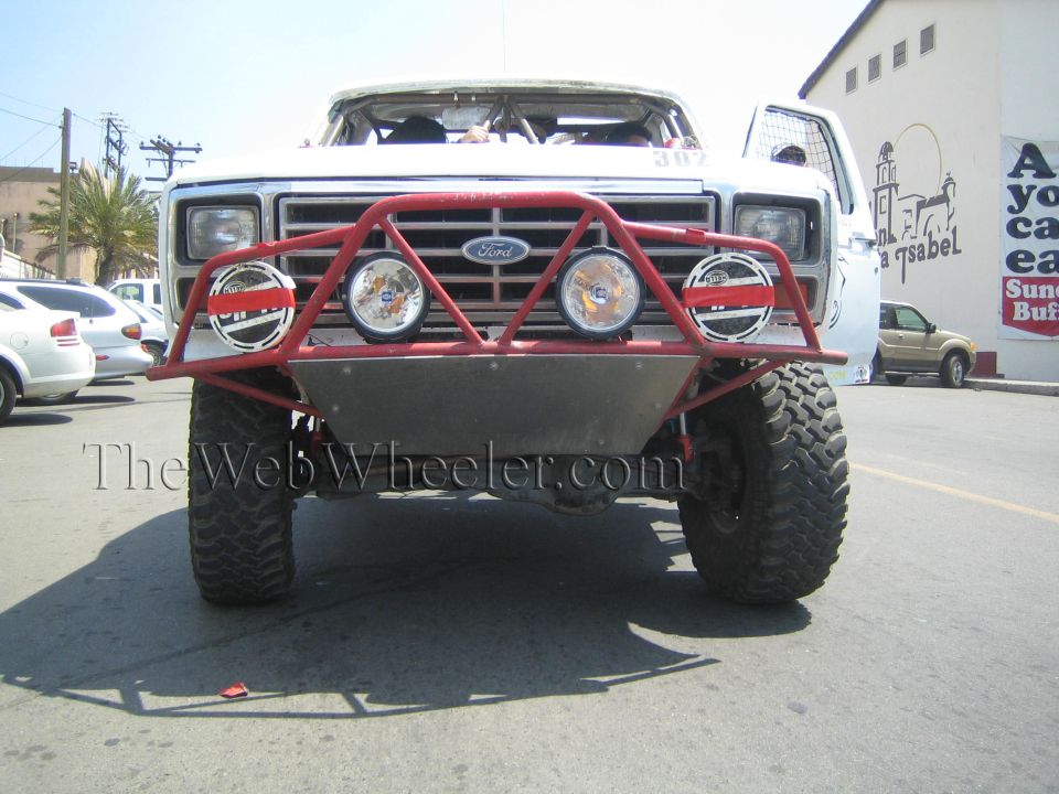 Front of white Ford race truck with red tube bumper and four round lights