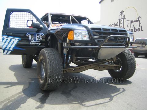 1990 Ford Bronco - black LS Racing prerunner pickup with a tubular front bumper and long-travel suspension sits with its door open on a street.