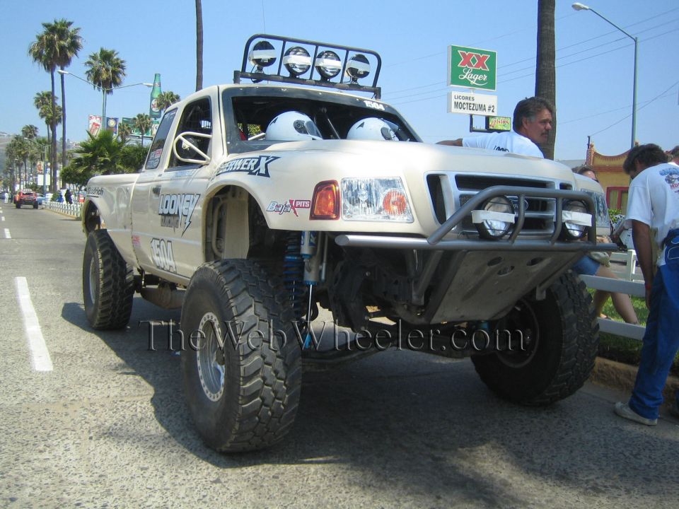 Tan Ford Ranger prerunner race truck with roof lights driving on a street lined with spectators