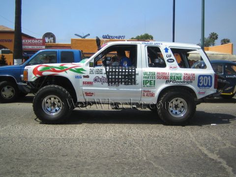 1990 Ford Bronco - Side profile of a white lifted Ford Explorer race SUV numbered 301, plastered with sponsor decals on a street.