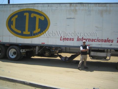 1990 Ford Bronco - man stands beside a white semi trailer bearing a large yellow 'LIT' logo, with a hammock hung beneath the trailer.