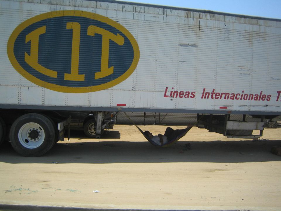 White semi trailer with large yellow LIT logo and a person resting in a hammock underneath