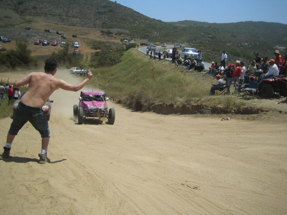 Pink off-road buggy descending a dirt hill as a shirtless man cheers it on