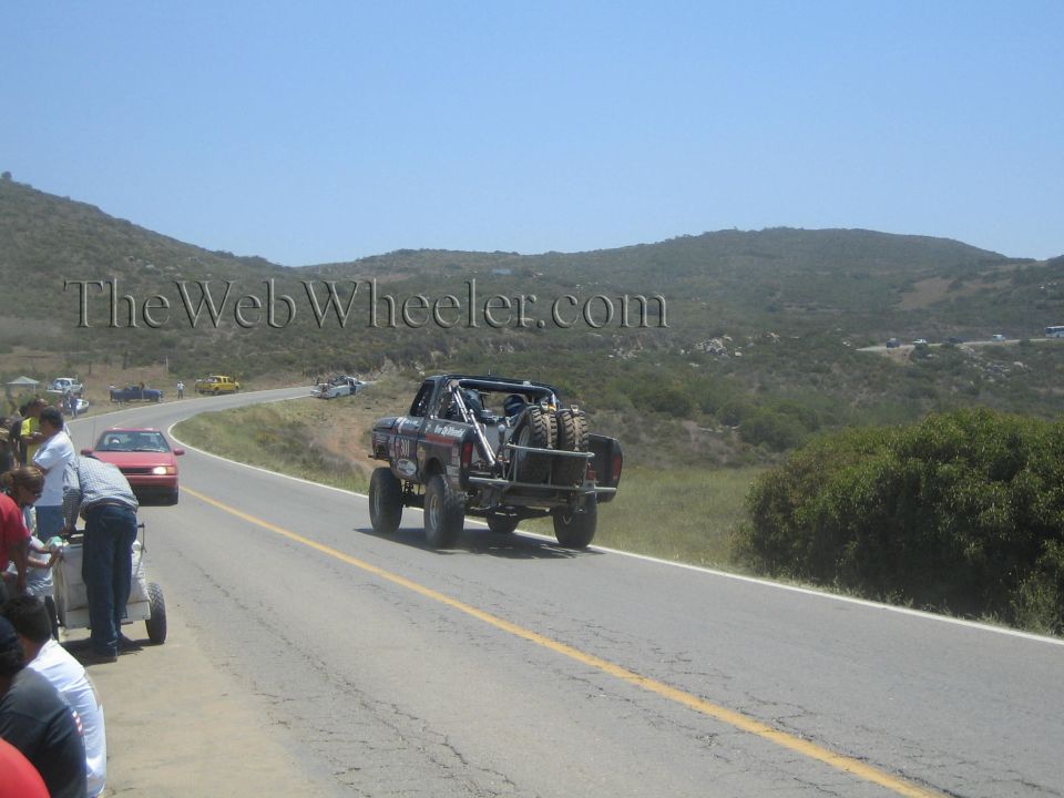 Lifted race truck carrying a spare tire heading away down a paved hill road
