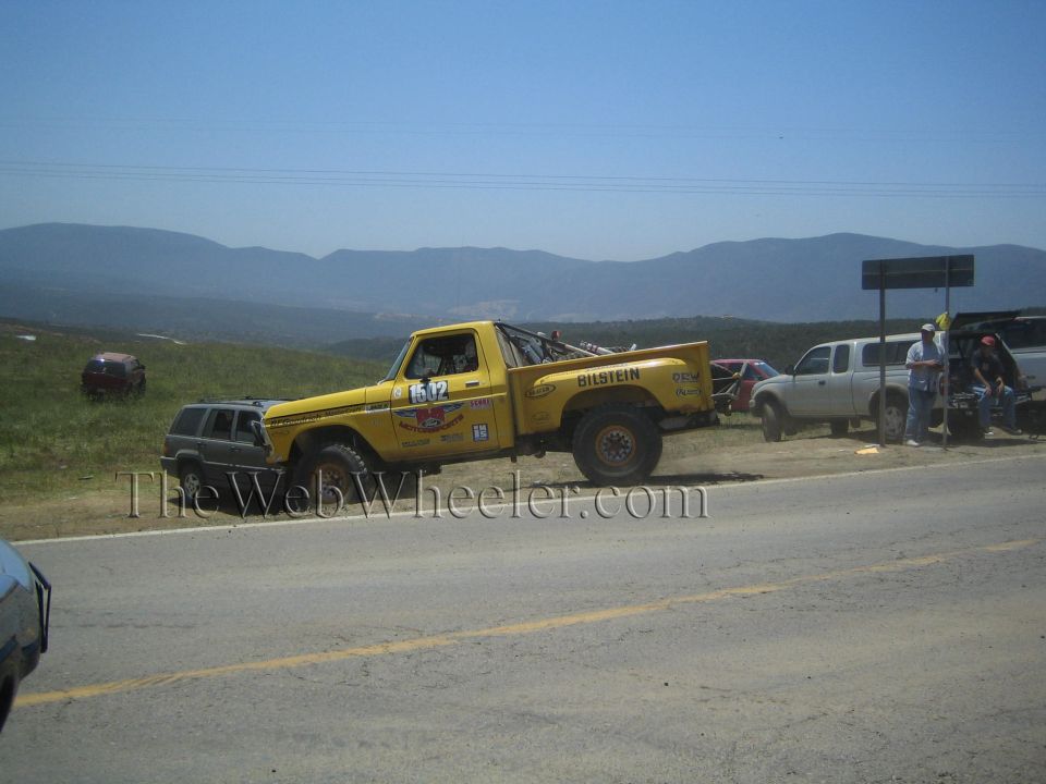 Yellow Ford number 1542 race truck parked on a roadside with mountain backdrop