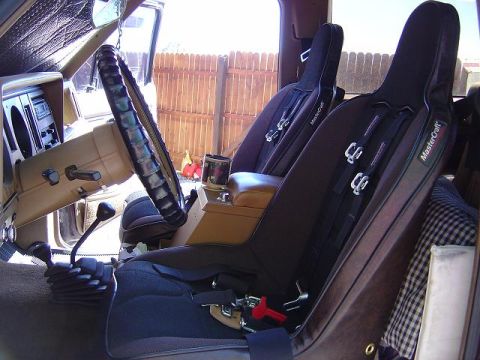 1986 Ford Bronco II - The interior of a vehicle shows racing seats, a steering wheel, and a manual shifter, with a wooden fence visible through the window.