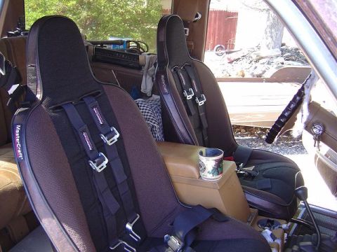 1986 Ford Bronco II - The interior of a vehicle shows two bucket seats equipped with racing harnesses and a cup holder on the center console.
