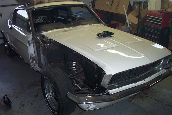 White 1967 Ford Mustang undergoing restoration, front fender removed, hood open