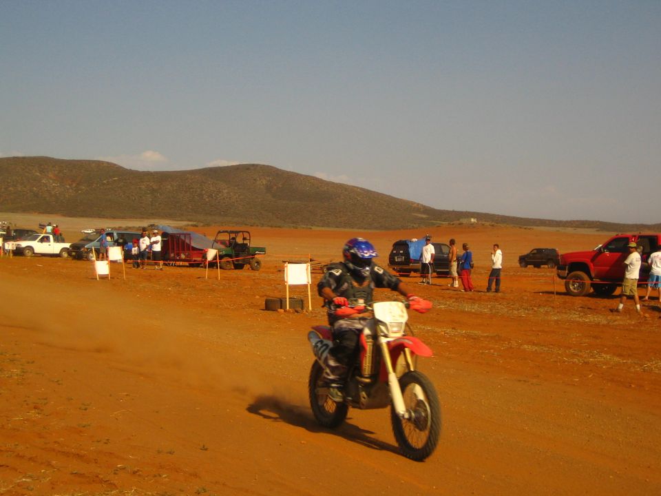 Helmeted rider on red Honda dirt bike racing a red dirt desert course