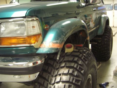 1996 Ford Bronco - The front fender of a green Ford Bronco is undergoing repair work, with large tires visible.