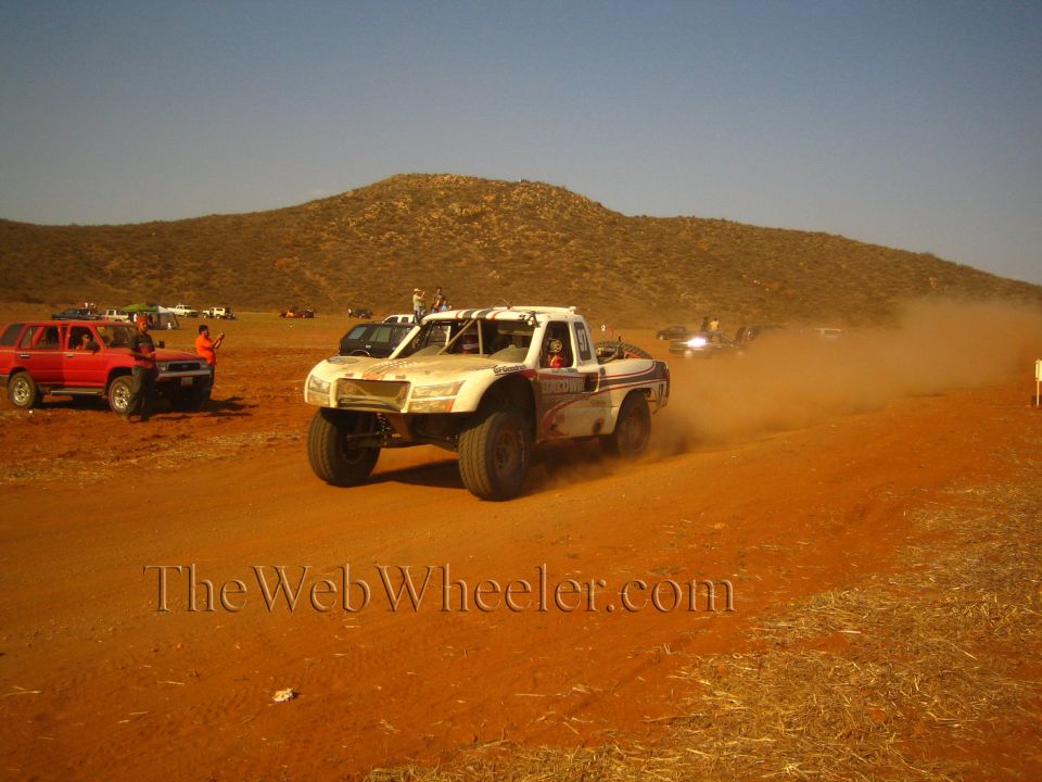 White and blue off-road race truck speeding on a red dirt desert course