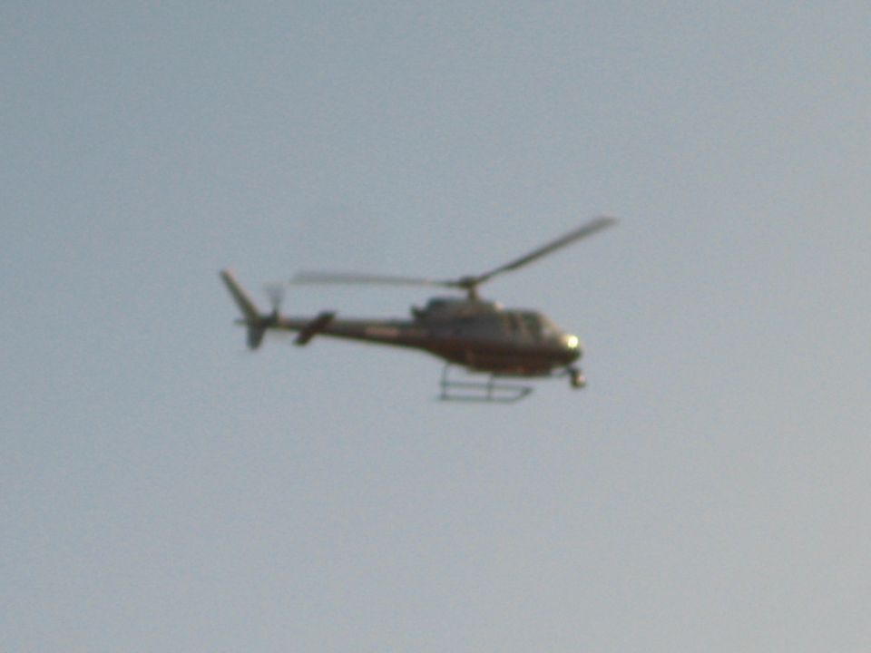 Small light-colored helicopter flying against a pale blue sky