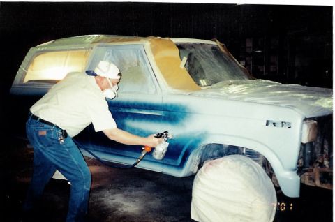 1981 Ford Bronco - A person is spray painting the fender of a 1981 Ford Bronco during a body shop process.