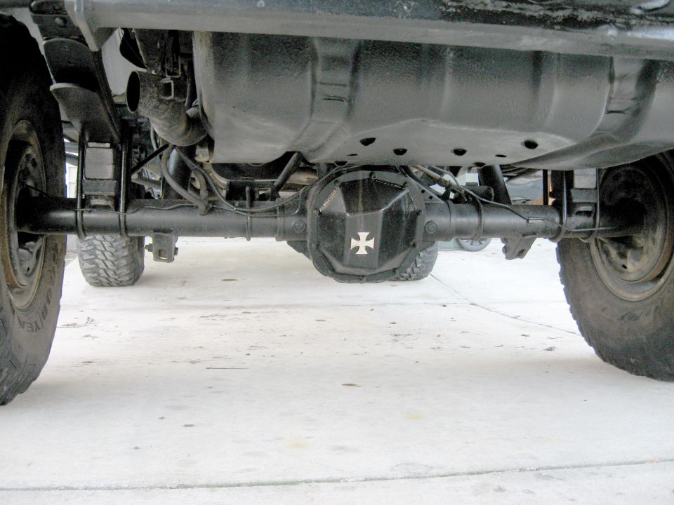 Underside view of a vehicle's rear axle assembly with a black differential cover a white cross emblem