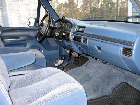 1996 Ford Bronco - The interior of a blue truck features a light blue dashboard and seats, with a view of the steering wheel and pedals.