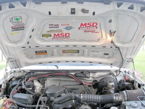 1996 Ford Bronco - The engine bay of a white vehicle displays numerous aftermarket performance stickers under the open hood.