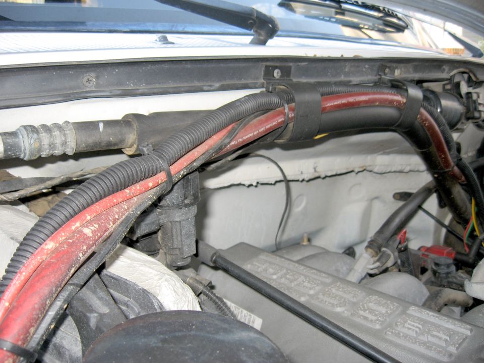 Heavy red battery cable and black loom routed along a firewall in an engine bay