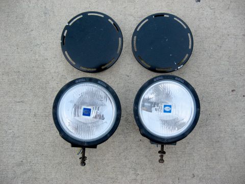 1996 Ford Bronco - Pair of Hella fog lights and their protective covers laid out on a concrete surface.